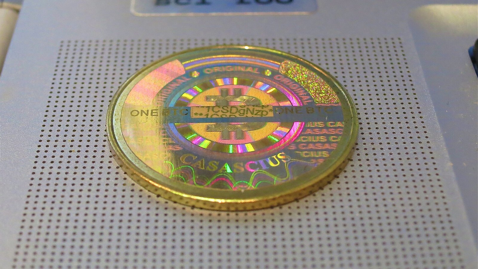 A Casascius physical bitcoin coin with a holographic seal resting on a device